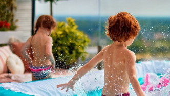 Two kids playing in paddling pool with fence around it.