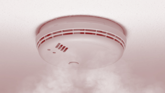 Smoke alarm installed in a ceiling with smoke circulating around it