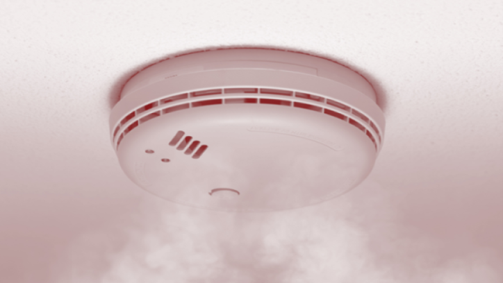 Smoke alarm installed in a ceiling with smoke circulating around it